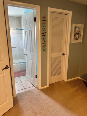 Un couloir avec une porte blanche donnant sur une salle de bain, un mur décoratif agrémenté d’éléments en bois et un tableau encadré accroché au mur.