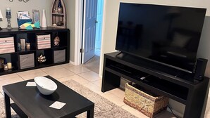 Una sala de estar con televisor, mueble de entretenimiento negro y una puerta con la etiqueta 'SEASHORE'.