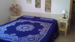 A bedroom with a large bed covered in a blue and white patterned bedspread, a bedside table with a lamp, and three wall-mounted paintings. - La Magione del Capitano (Montecorvino Pugliano)