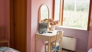 A bedroom with a bed, a desk with a computer, a chair, a window with a view of greenery, and a wardrobe. - La Magione del Capitano (Montecorvino Pugliano)