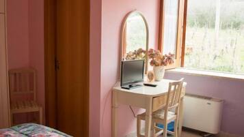 Una camera da letto con un letto, una scrivania con un computer, una sedia, una finestra vista su del verde e un armadio.