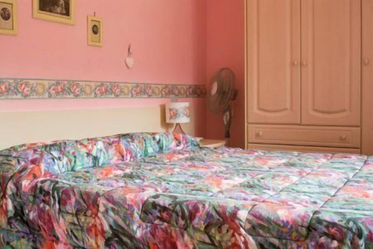 Un dormitori amb llençols estampats, una taula de nit amb una làmpada i un armari.