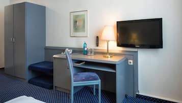 A hotel room with a bed, a desk with a chair, a television, a lamp, and a remote control.