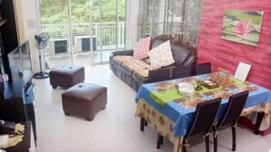 Uma sala de estar moderna com sofá, pufes, uma mesa de jantar com cadeiras e uma grande janela com vista para o verde.