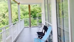 Uma varanda com vista para vegetação, um corrimão branco e duas cadeiras azuis.