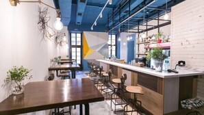 A modern cafe with wooden tables and chairs, a bar area, and shelves with plants and kitchen items. - Dream Hostel Lviv (Lviv)