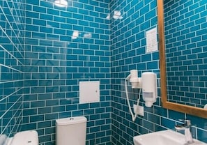A bathroom with blue-tiled walls, a white sink, a mirror, and a hand dryer. - Dream Hostel Lviv (Lviv)