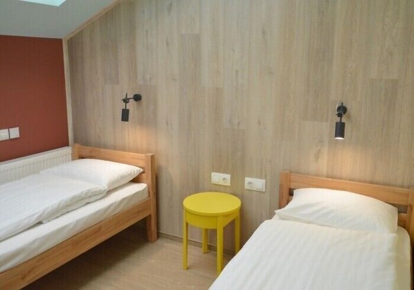 A room with two single beds, a small yellow table, and wooden panel walls. - Dream Hostel Lviv (Lviv)