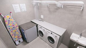 A compact laundry room with a washing machine, dryer, ironing board, and a sink. - Dream Hostel Lviv (Lviv)