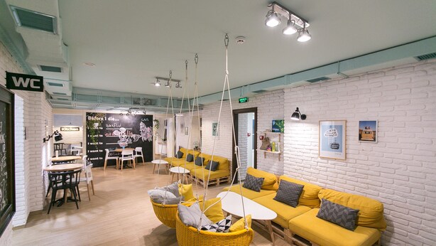 A modern interior with a yellow sofa, hanging chairs, and a kitchen area. - Dream Hostel Lviv (Lviv)