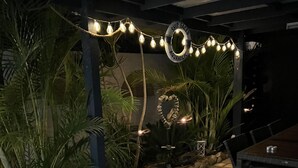 An outdoor patio area with a brick pathway, wicker furniture, string lights, and tropical plants. - Bayview water front holiday rental. (Lemon Tree Passage)