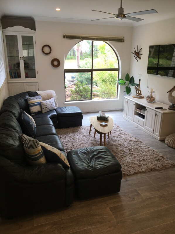 Uma sala de estar com sofá de couro preto, um armário branco, uma janela redonda e um ventilador de teto.