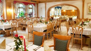A dining area with multiple tables and chairs, a cross on the wall, and a large arched window. - Hotel Sonnenblick (Staffelstein)