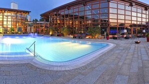 A swimming pool with a glass enclosure, surrounded by a paved area with lounge chairs and a building with large windows. - Hotel Sonnenblick (Staffelstein)