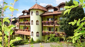 A multi-story building with balconies adorned with flowers, a prominent tower, and a surrounding garden. - Hotel Sonnenblick (Staffelstein)