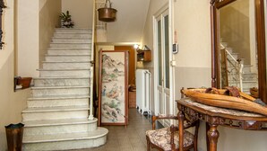 A staircase with a chandelier, a dining table with chairs, and a large mirror.