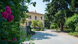 A building with a gravel driveway, surrounded by lush greenery and flowering plants.