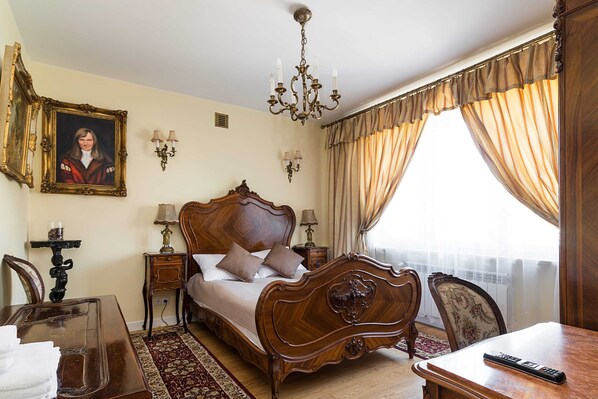 A traditional bedroom with a large bed, a chandelier, a desk, and a chair. - At the Fountain Apartment (Warsaw)