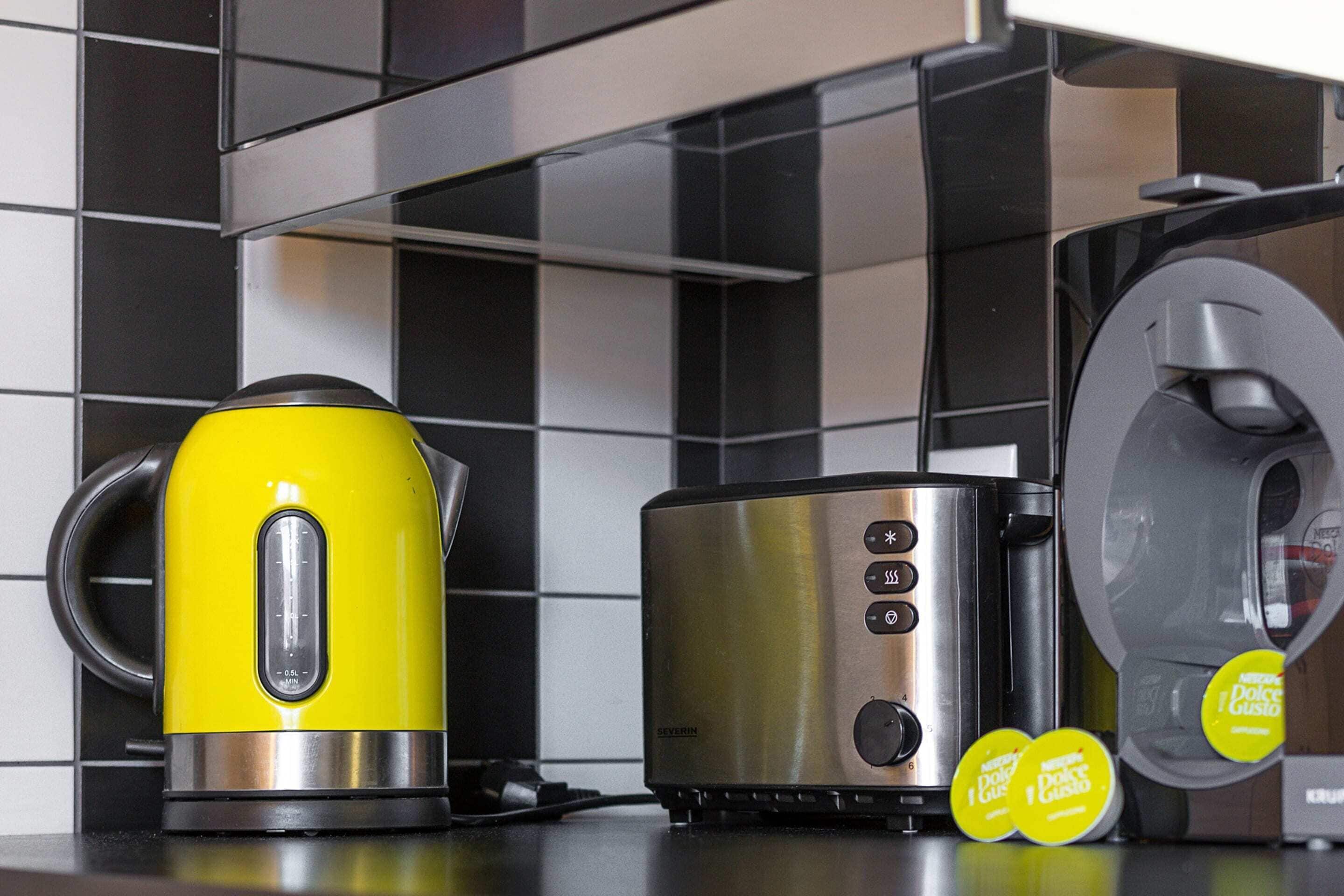 A kitchen with a yellow kettle, a stainless steel toaster, and a coffee machine.