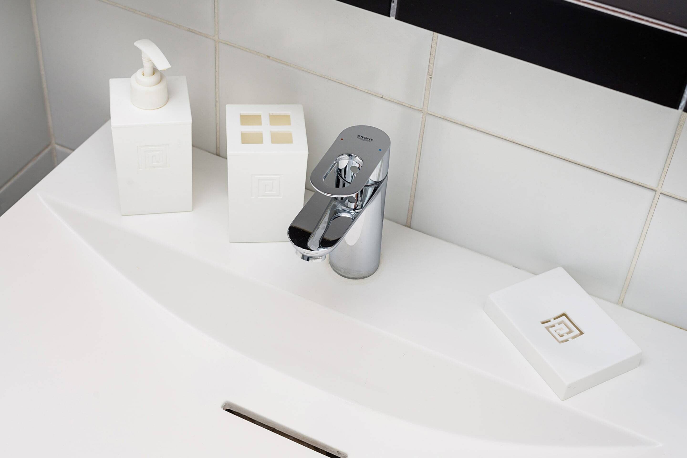 A bathroom with a white sink, a chrome faucet, a soap dispenser, and a small white box with a geometric design.