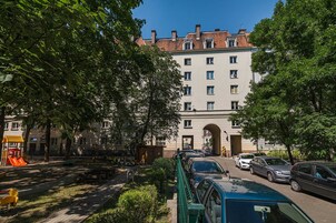 Un edificio de varios pisos con un arco de entrada central, rodeado de coches estacionados y un parque infantil con un tobogán.