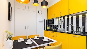 A modern kitchen with yellow cabinets, a black countertop, and a dining area with a table set for two. - At the Fountain Apartment (Warsaw)
