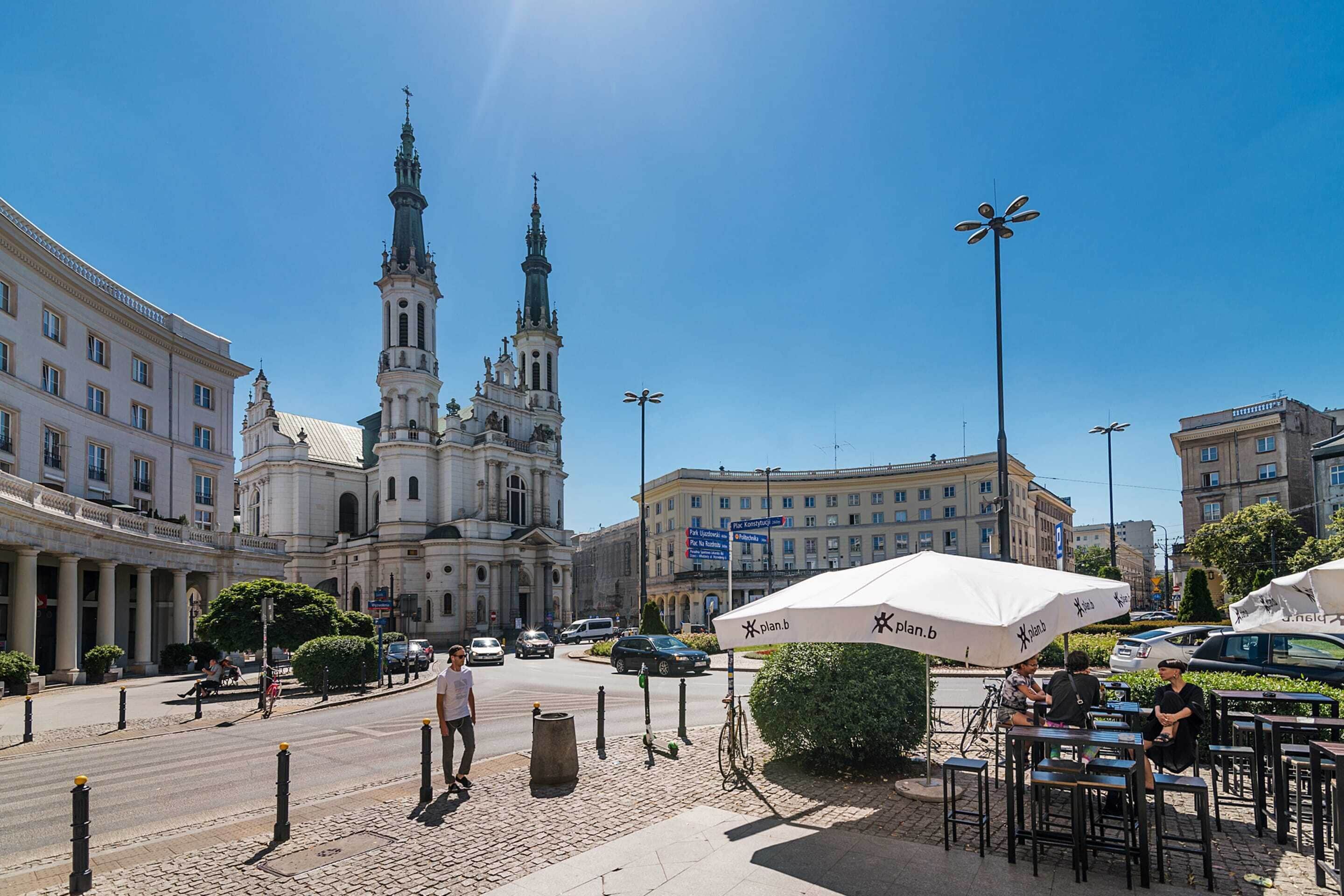 A city square with a prominent church, outdoor seating, and a clear blue sky.