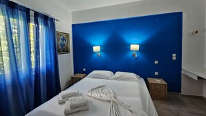 A hotel room with a large bed, two bedside tables, a blue accent wall, and a painting on the wall. - Corfu Island Apartment 148 (Corfu)