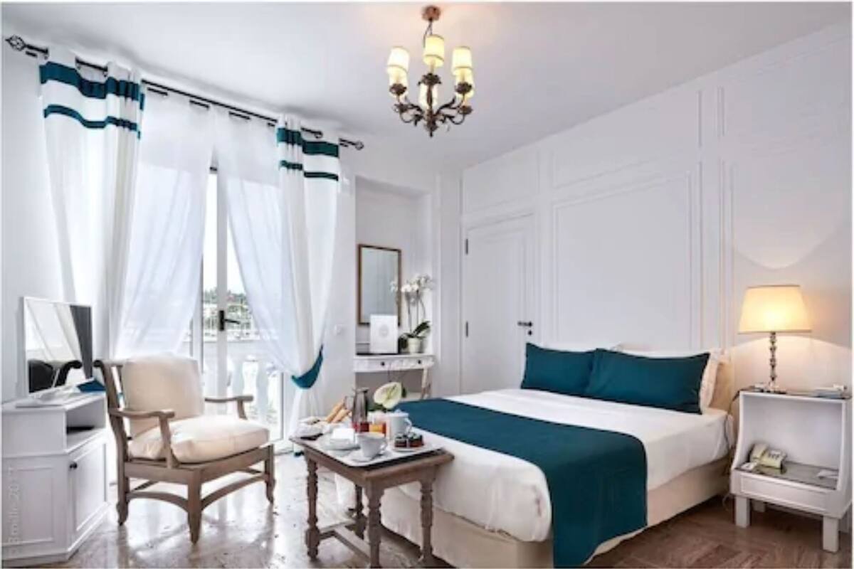 A hotel room with a bed, a chair, a bedside table, a lamp, and a window with curtains.