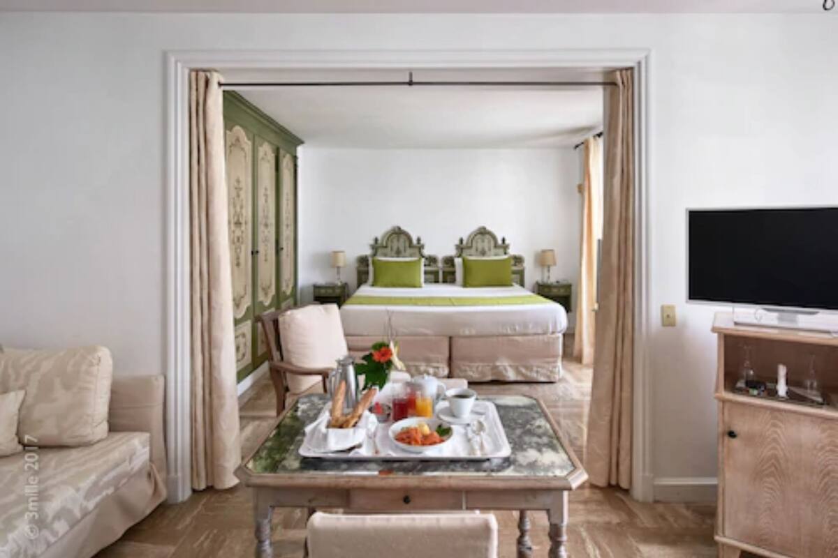 A hotel room with a bed, a dining table with breakfast, a TV, and a wooden cabinet.