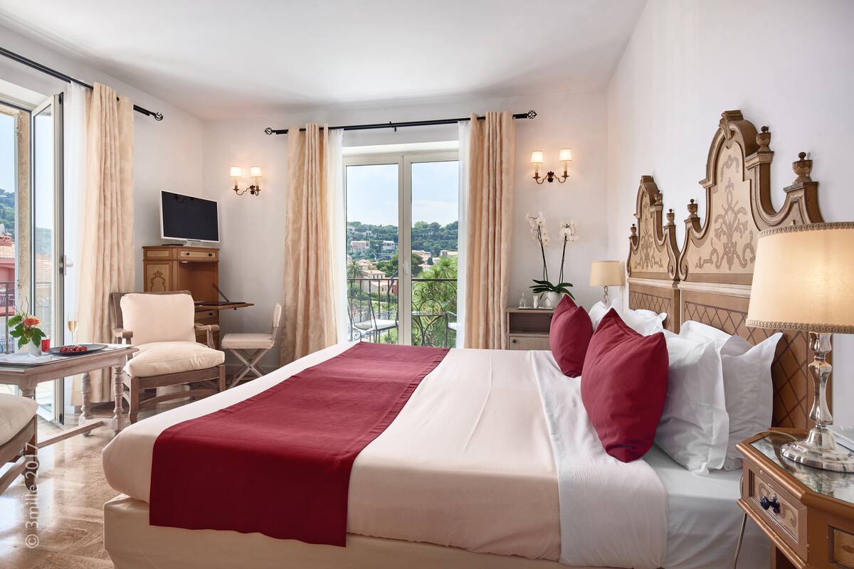A hotel room with a large bed, a TV, a desk, and a view of the city.