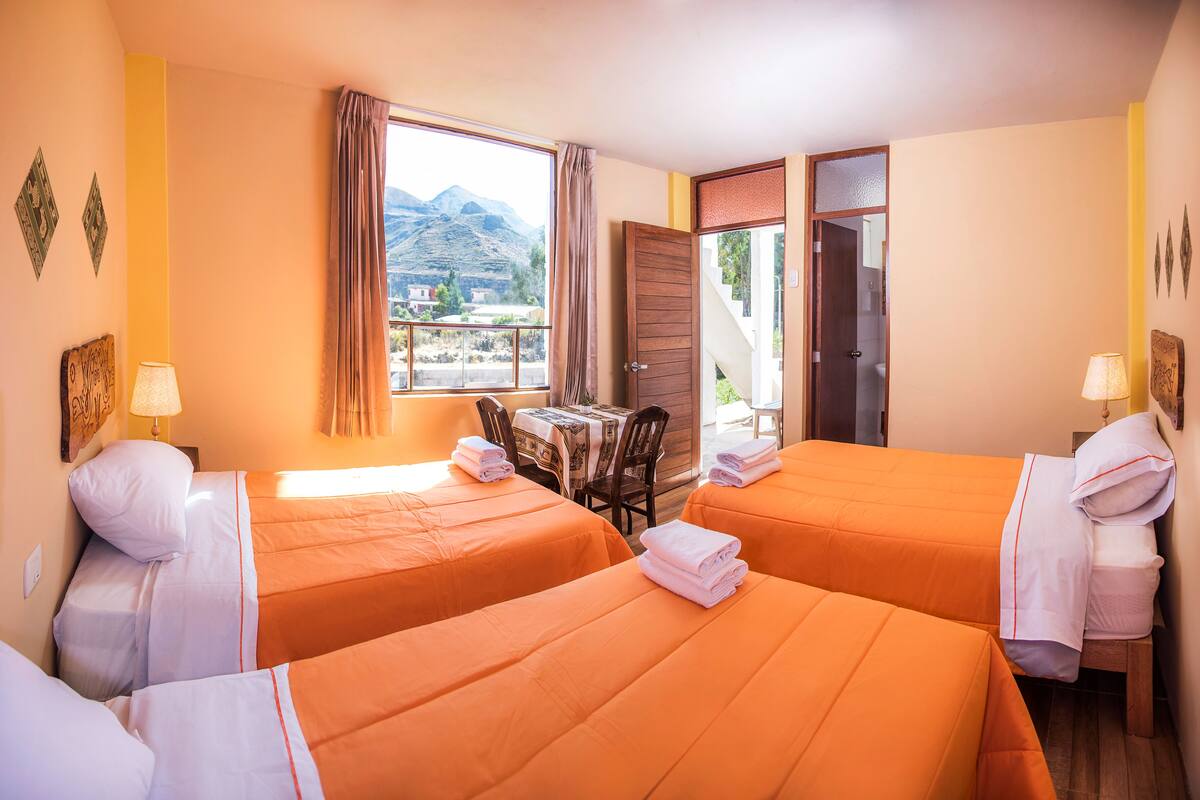 Habitación de hotel con dos camas, una mesa y vistas a las montañas.