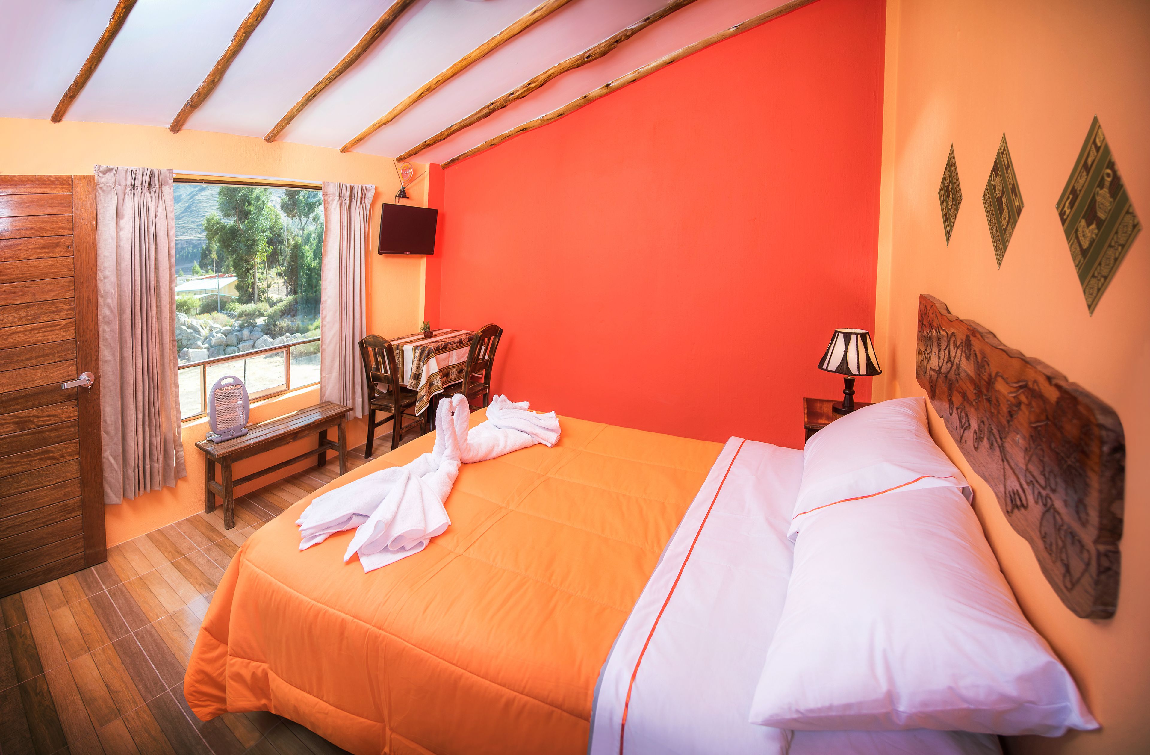 Habitación de hotel con cama, banca de madera, mesa y televisor en la pared.