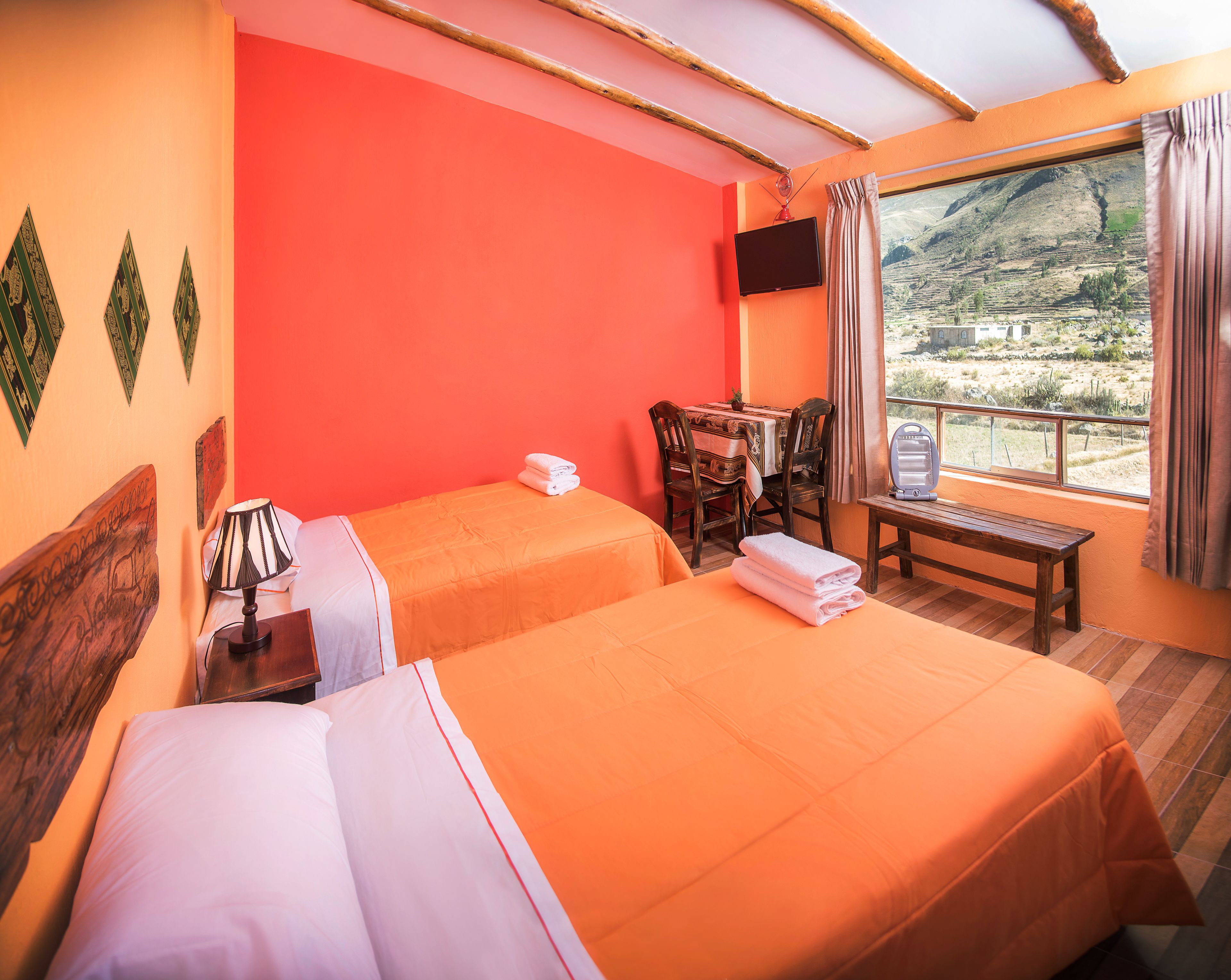 A hotel room with two beds, a table, chairs, a TV, and a window with a mountain view.
