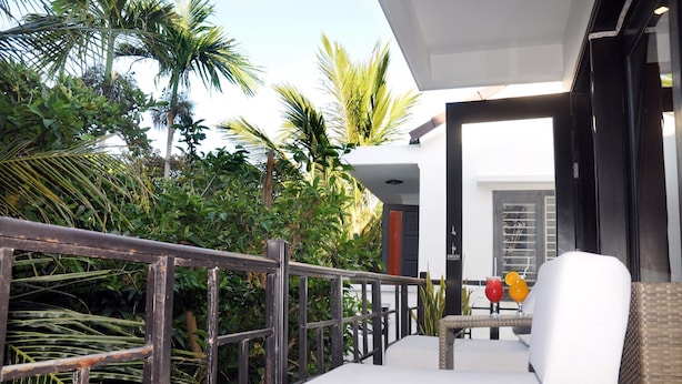 Un balcon doté d’un espace salon avec des coussins blancs, d’une rambarde en métal et d’une table avec des boissons.