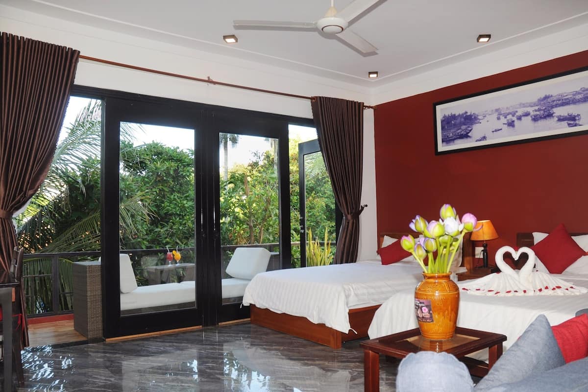 A hotel room with a bed, a vase of flowers, a painting, and a balcony with a view of greenery.