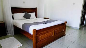Una cama de madera con una colcha blanca y gris, un almohón gris y una cortina blanca.