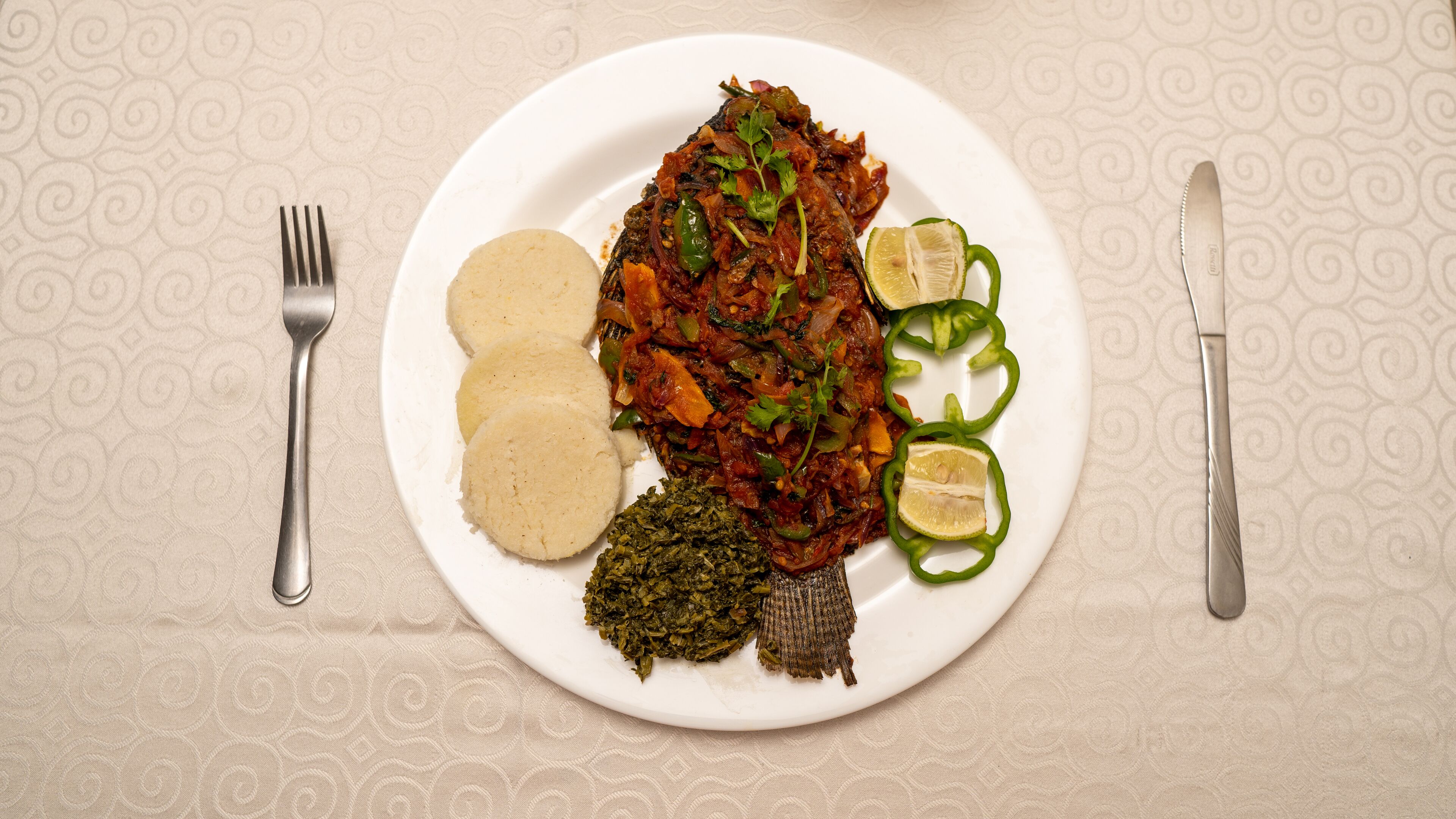 A plate with a fish dish, three round items, a green vegetable, and lime slices.