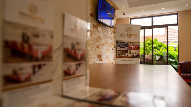 Un área de recepción con pared de ladrillo, un televisor sobre el mostrador de recepción y un cartel del Hotel Whirlspring.