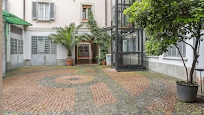 Ein Innenhof mit Kopfsteinpflasterweg, Blumentöpfen und einem Gebäudeeingang.