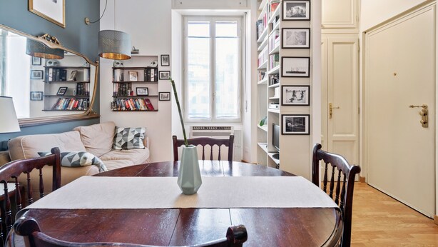 A dining area with a wooden table, chairs, a vase, and a bookshelf with framed pictures. - Flatty Apartments Garigliano (Milan)