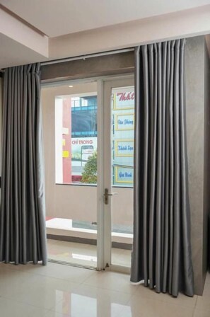Habitación de hotel con puerta de vidrio corredera que da a un balcón, piso de baldosas y vista a la calle.