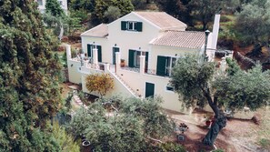 A two-story house with a balcony, surrounded by trees and vegetation. - Villa Costa (Corfu)
