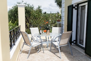 A patio with a round table and four chairs, surrounded by a metal fence and greenery. - Villa Costa (Corfu)