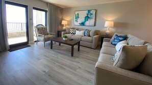 A modern living room with a sofa, armchair, coffee table, and two lamps. There is a balcony with a view outside. - Breakers East 1202- Gulf Front Spacious 2 BR/2BA Beach setup included (Destin)