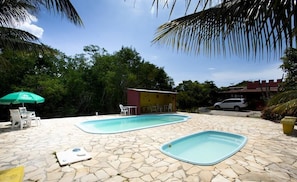 A swimming pool area with two pools, stone flooring, and outdoor seating. - Pousada dos Gravatais (Marataizes)
