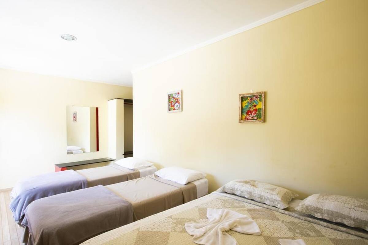 Una habitación de hotel con dos camas individuales, una mesita de noche, un espejo y dos cuadros en la pared.