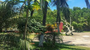 Un giardino tropicale con palme, una scultura a forma di uccello bianco e un edificio rosso sullo sfondo.