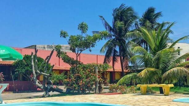 Una piscina con bordo piastrellato, circondata da palme e un edificio con tetto rosso.