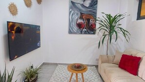 Ein Wohnzimmer mit Flachbildfernseher, einem Gemälde, einem gemusterten Teppich, einer Couch und zwei Zimmerpflanzen.